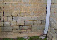 A granite block building suffering from accelerated erosion of the weakened mortar at the base of the building. Note also mechanical breakdown and staining of the granite blocks.